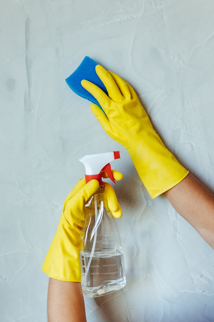 home-hero-bg Hands in yellow gloves cleaning wall with sponge and spray bottle.